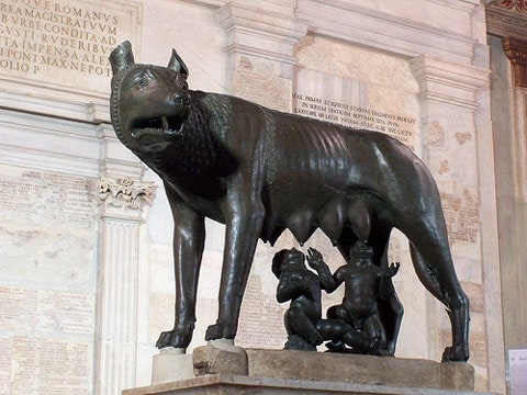 Před Kapitolským náměstím (Piazza del Campidoglio) na sloupu kojí kapitolská vlčice La Lupa Capitolina malého Romula a Rema